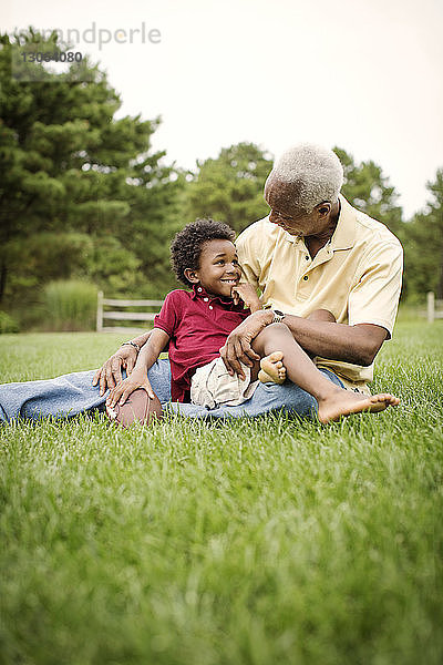 Grossvater und Enkel unterhalten sich  während sie auf einem Grasfeld im Hinterhof sitzen