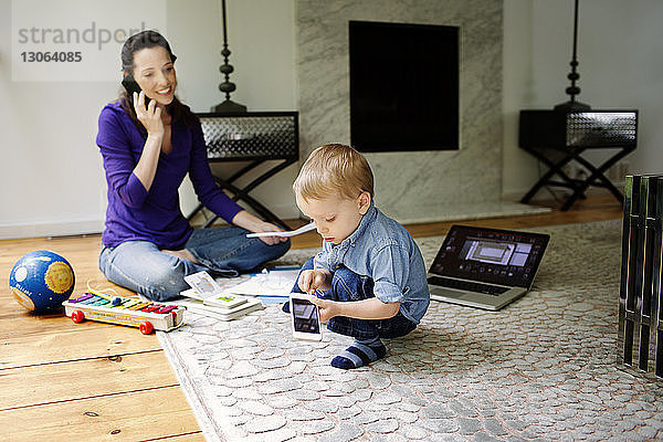 Sohn spielt mit der Technik  während die Mutter zu Hause telefoniert und Papierkram erledigt