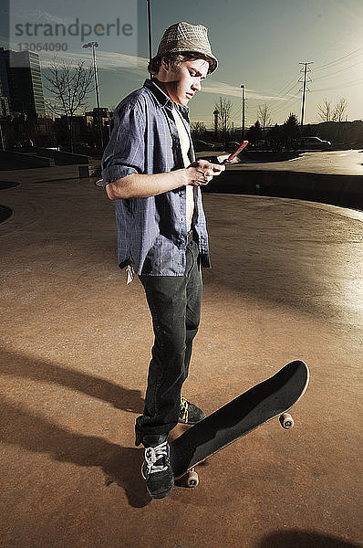 Mann benutzt Mobiltelefon  während er mit Skateboard auf der Sportrampe steht