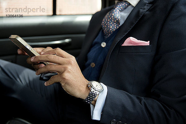 Ausgeschnittenes Bild eines Geschäftsmannes  der ein Mobiltelefon benutzt  während er im Auto sitzt
