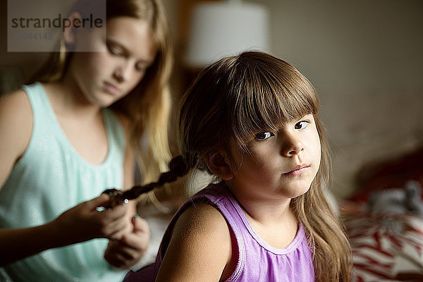 Mädchen flechtet der Schwester die Haare  während sie zu Hause auf dem Bett sitzt