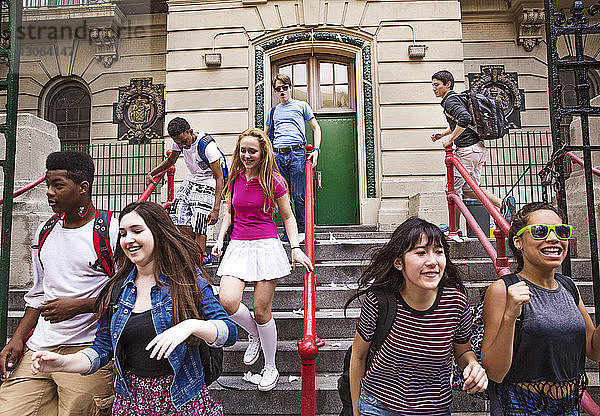 Glückliche Schülerinnen und Schüler bewegen sich auf Stufen vor der High School nach unten