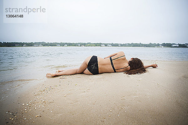 Rückansicht einer am Strand im Sand liegenden Frau