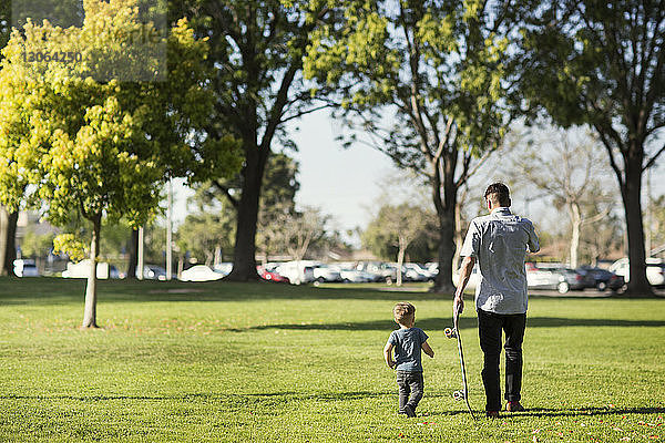 Rückansicht von Vater und Sohn beim Spaziergang auf einem Grasfeld