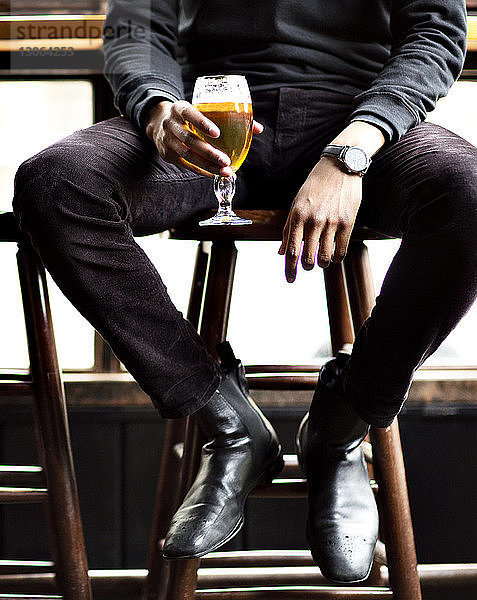 Niedriger Teil eines Mannes  der Weinglas hält  während er auf einem Hocker in einer Bar sitzt
