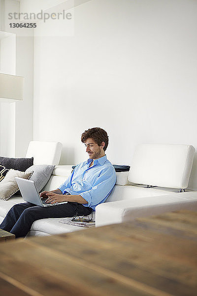 Geschäftsmann benutzt Laptop-Computer  während er zu Hause auf dem Sofa sitzt