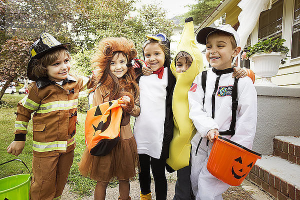 Fröhliche Kinder in Halloween-Kostümen  die während eines Streichs oder einer Behandlung im Hof stehen