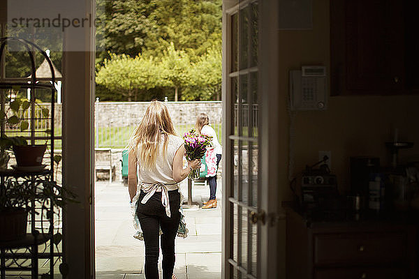 Rückansicht einer Frau  die eine Blumenvase trägt  während sie auf dem Rasen geht  durch die Tür gesehen