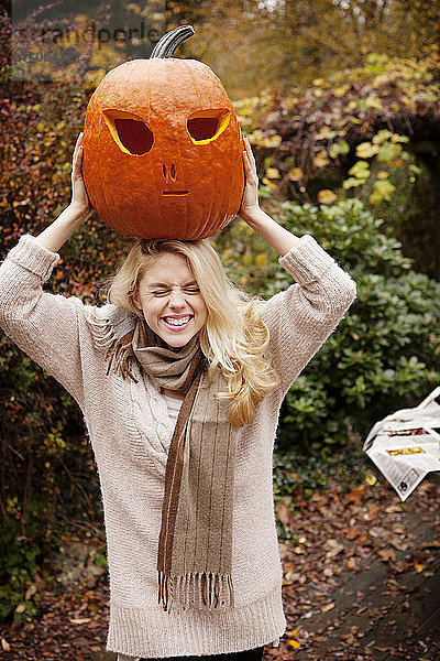 Frau trägt Halloween-Kürbis auf dem Kopf  während sie im Hinterhof steht