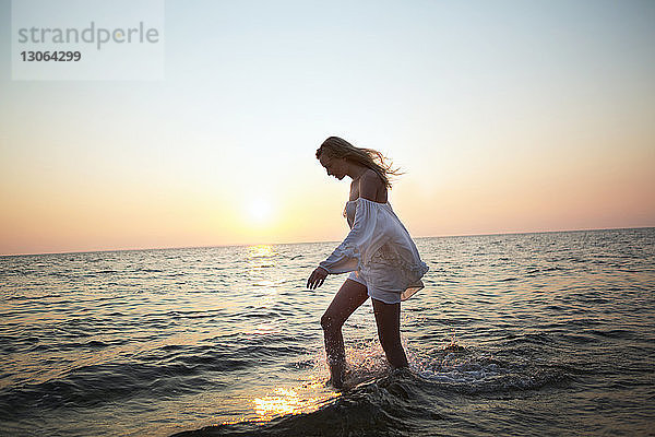 Seitenansicht einer Frau  die am Strand gegen klaren Himmel im Wasser geht