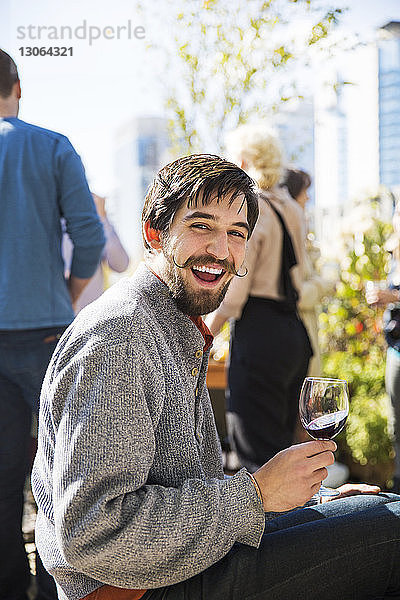 Porträt eines fröhlichen Mannes  der während einer Gartenparty ein Rotweinglas hält