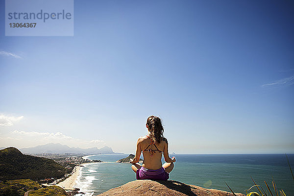 Frau meditiert  während sie auf einem Felsen am Meer sitzt