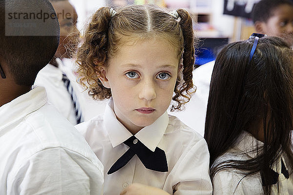 Porträt eines Schulmädchens  das mit Klassenkameraden im Klassenzimmer steht