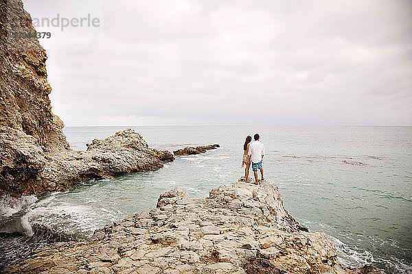 Rückansicht eines auf einem Felsen am Strand stehenden Paares