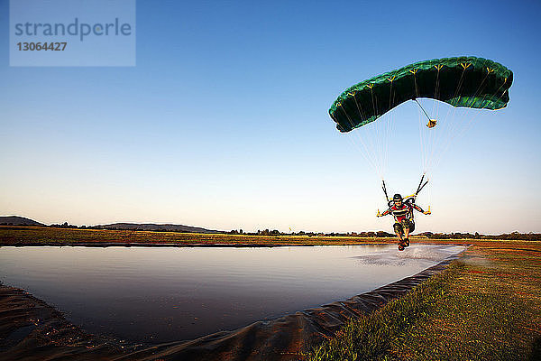 Mann segelt mit dem Fallschirm über den See gegen klaren Himmel