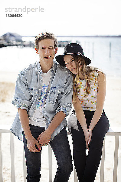 Porträt eines Paares  das auf einem Geländer am Pier vor dem Strand sitzt