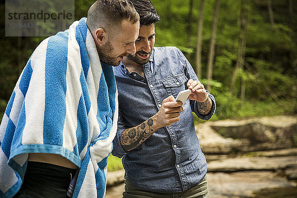 Mann zeigt seinem Freund sein Handy  während er im Wald steht