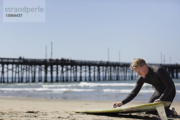 Mann bereitet sich am Strand kniend auf das Surfen vor