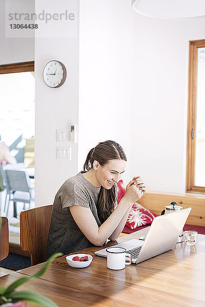 Glückliche Frau schaut auf Laptop-Computer  während sie zu Hause sitzt