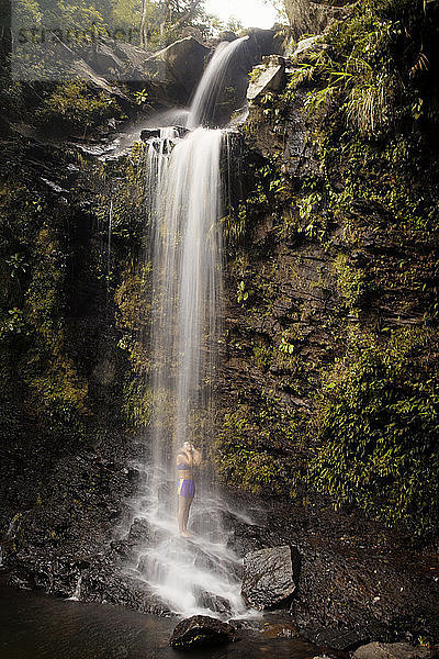 Eine Frau geniesst unter einem Wasserfall  der über eine Felsformation fliesst