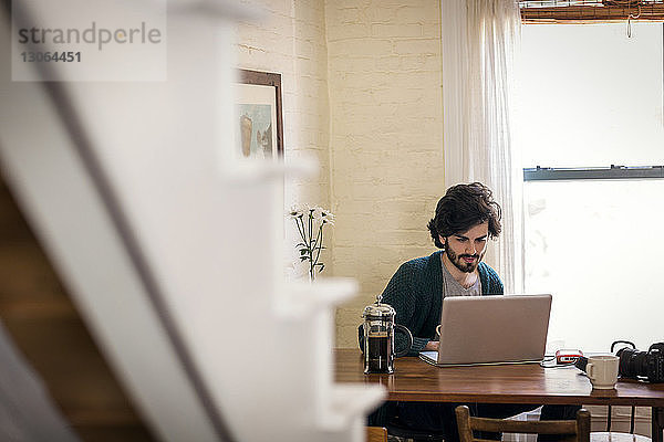 Mann benutzt Laptop-Computer  während er zu Hause sitzt