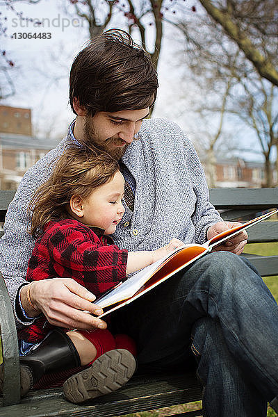 Vater und Tochter lesen Buch  während sie auf einer Parkbank sitzen