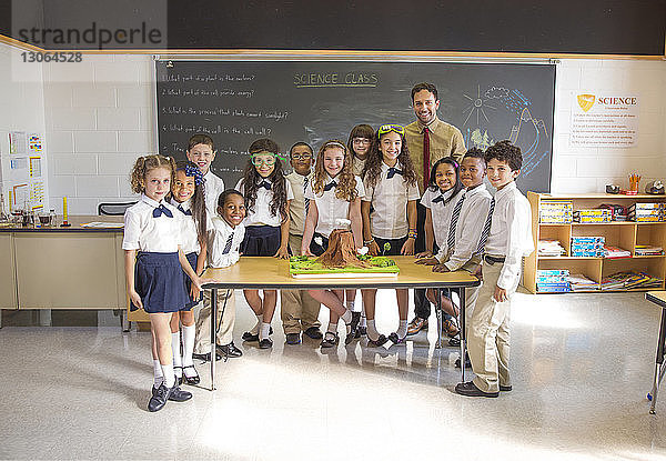 Porträt von Schülern mit am Schreibtisch stehendem Lehrer im Klassenzimmer
