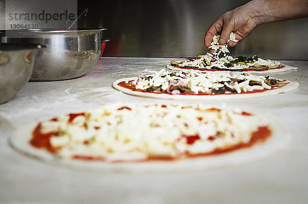 Beschnittenes Bild einer Hand  die Käse auf Pizza legt