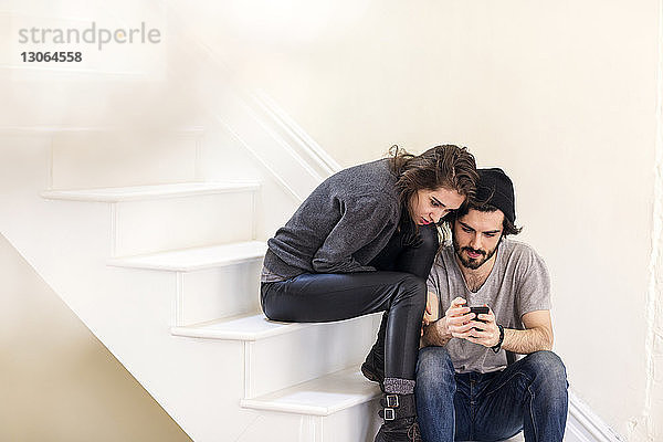 Ehepaar betrachtet Smartphone  während es auf der Treppe sitzt