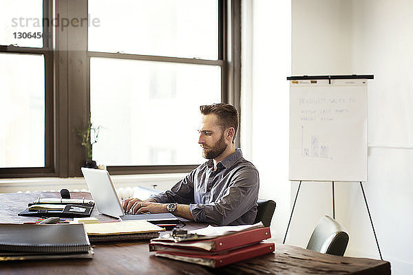Mann arbeitet am Laptop-Computer  während er im Büro am Schreibtisch sitzt
