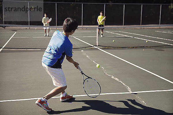 Jungen spielen an sonnigen Tagen Tennis auf dem Platz gegen den Zaun