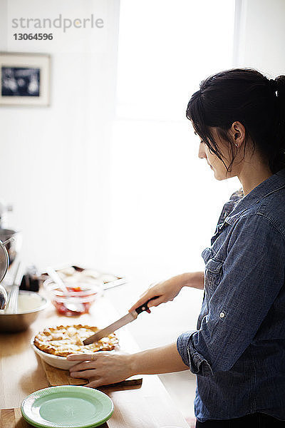 Seitenansicht einer Frau  die Kuchen schneidet  während sie zu Hause an der Küchentheke steht