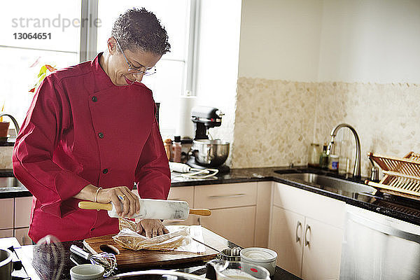 Frau zerkleinert Tortenzutat mit Nudelholz bei der Arbeit in der Küche zu Hause