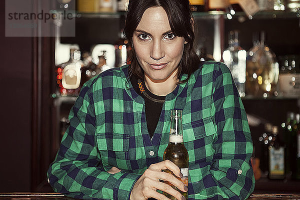 Porträt einer Frau  die zu Hause eine Bierflasche hält