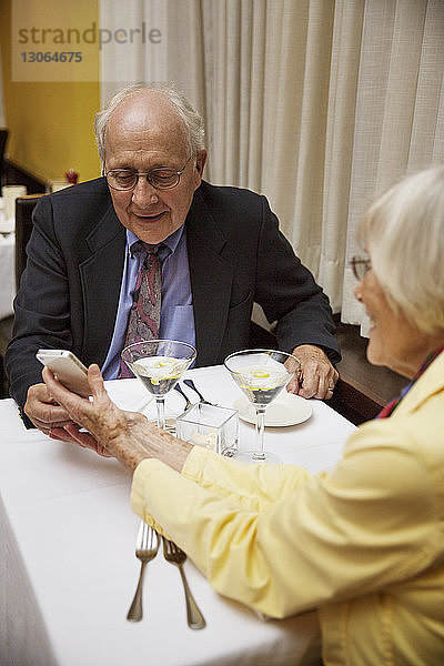 Ältere Frau zeigt einem Mann ein Smartphone  während sie im Restaurant sitzt