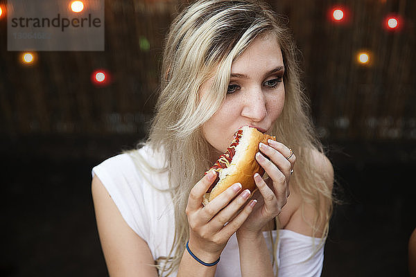Frau mit blonden Haaren isst Hot Dog auf Gartenparty