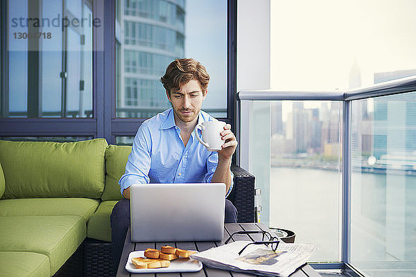 Geschäftsmann benutzt Laptop beim Kaffee trinken auf dem Balkon des Büros