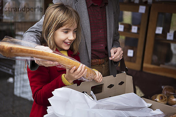 Mitschnitt einer Frau mit lächelnder Enkelin  die einen Laib Brot im Supermarkt hält