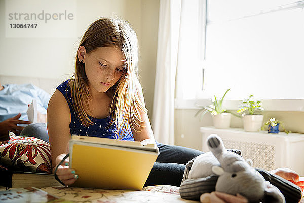 Mädchen benutzt Tablet-Computer  während sie sich zu Hause im Bett entspannt