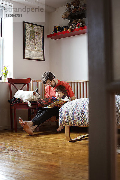 Vater und Tochter lesen Buch  während sie mit Hund zu Hause sitzen