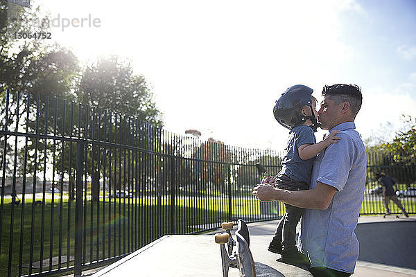 Seitenansicht eines Vaters  der seinen Sohn im Skateboard-Park küsst