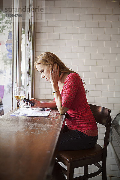 Seitenansicht einer Frau  die ein Smartphone benutzt  während sie im Restaurant sitzt