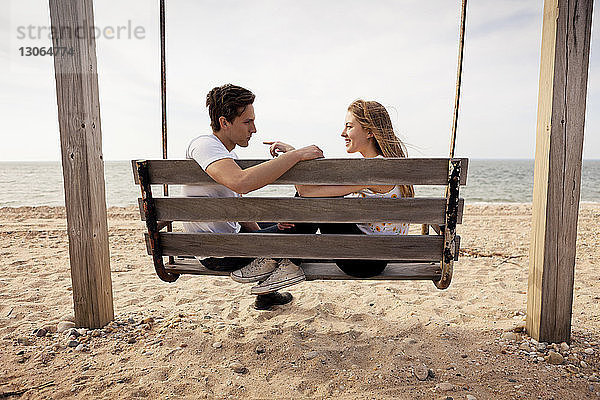 Seitenansicht eines am Strand auf einer Schaukel sitzenden Paares