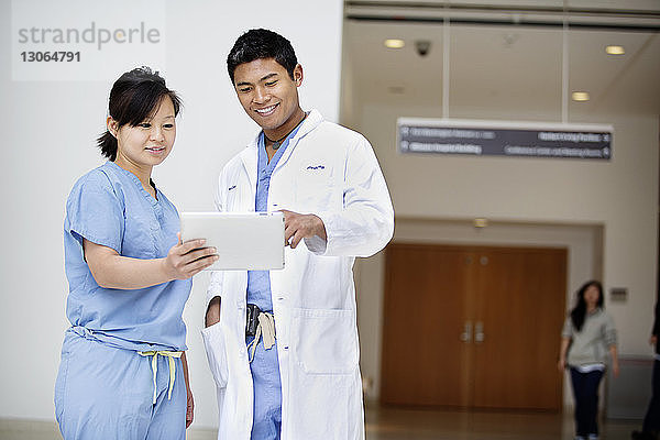 Lächelnde Ärzte schauen auf Tablet-Computer  während sie im Krankenhaus stehen
