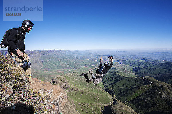 Mann sieht Freund beim Öffnen des Fallschirms an  während er auf dem Berg steht