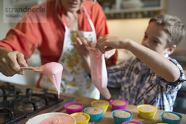 Frau mit Enkel füllt Cupcake-Halter in der Küche