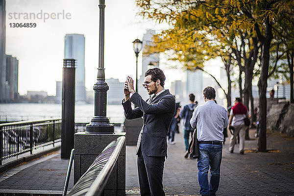 Geschäftsmann fotografiert mit einem Smartphone  während er auf einer Promenade in der Stadt steht