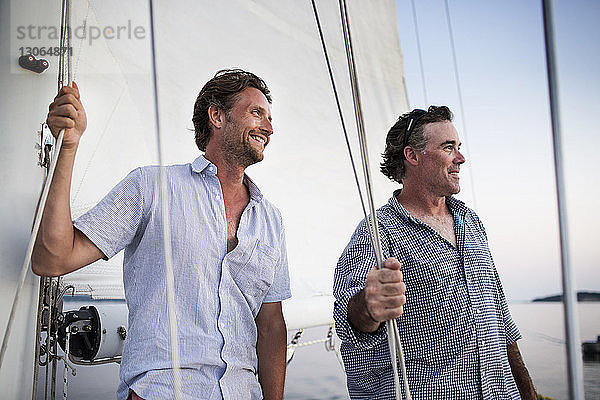 Seitenansicht eines glücklichen Mannes  der ein Seil bindet  während er auf einer Yacht steht