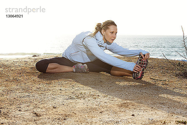 Frau berührt Zehen beim Sport am Strand