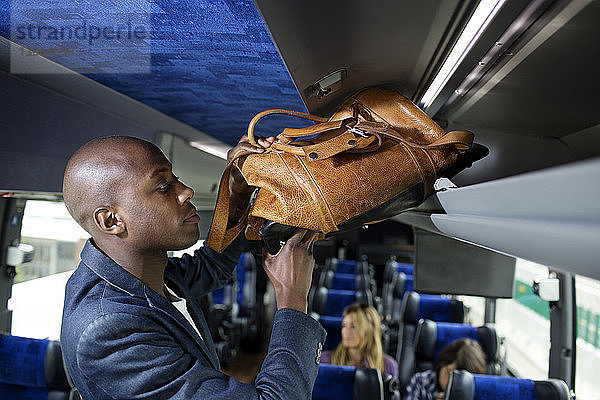 Mann legt Tasche in Gepäckträger im Bus